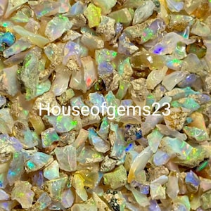 May include: A close-up of a pile of iridescent opal chips. The chips are of various sizes and shapes, with a mix of white, grey, and yellow tones. The opal chips are a popular choice for jewellery making and other crafts.