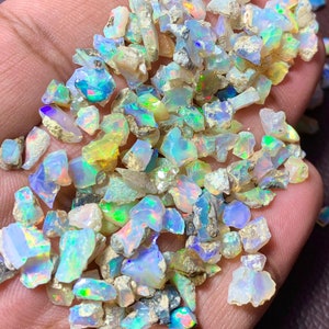 May include: A collection of small, iridescent opal chips in various shades of blue, green, and white. The chips are irregular in shape and have a rough, natural texture.