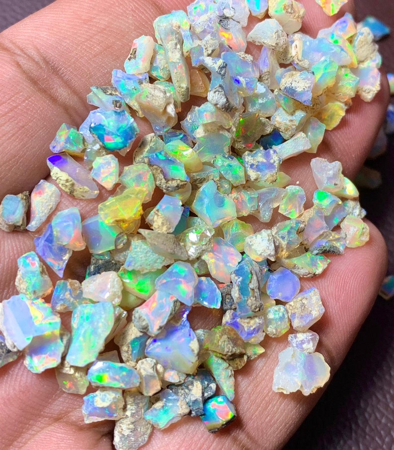 May include: A collection of small, iridescent opal chips in various shades of blue, green, and white. The chips are irregular in shape and have a rough, natural texture.