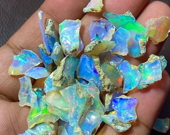 May include: A collection of rough opal gemstones in various shades of blue, green, and white. The opals are iridescent and have a natural, raw appearance.