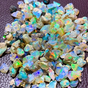 May include: A large pile of rough, iridescent opal gemstones in various shades of blue, green, and white. The opals are raw and have a natural, earthy look.