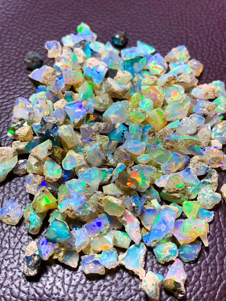 May include: A large pile of rough, iridescent opal gemstones in various shades of blue, green, and white. The opals are raw and have a natural, earthy look.