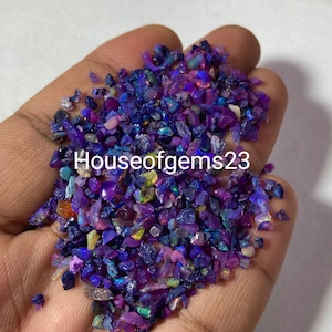 May include: Close-up of a handful of crushed opal gemstones. The opals are a mix of deep blues, purples, and iridescent colors. The text "Houseofgems23" is visible on the image.