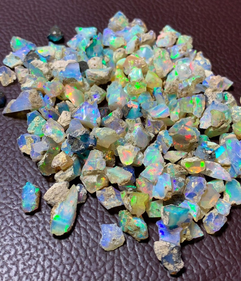 May include: A pile of rough, iridescent opal gemstones in various sizes and shapes. The opals are a mix of white, blue, green, and yellow.