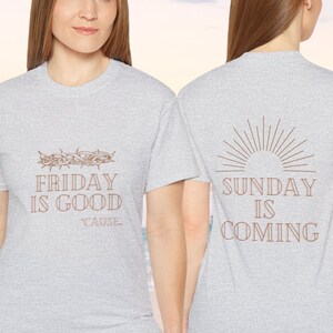 Op de afbeelding: Twee grijze T-shirts met een religieus thema. Het voorste shirt heeft een doornenkroon en de tekst "FRIDAY IS GOOD 'CAUSE". Het achterste shirt heeft een zonnestralen en de tekst "SUNDAY IS COMING".