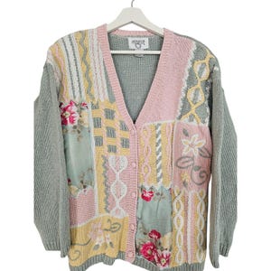 May include: A long-sleeve knit cardigan featuring a patchwork design in pastel pink, yellow, and sage green. The garment includes cable knit textures, ribbed trim, a V-neckline, button front closure, and floral fabric panels with the label Cervelle.