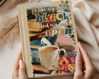 Może przedstawiać: Książka z napisem "I like my coffee BLACK and my books OPEN" jest trzymana w dłoniach. Okładka przedstawia filiżankę kawy, kwiaty i książki. Obraz ma ciepłą estetykę ze świecami i elementami dekoracyjnymi.