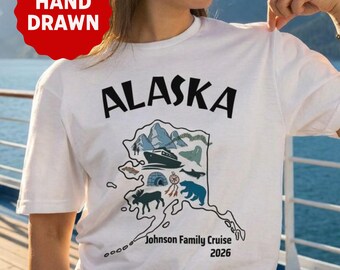 Może przedstawiać: Biały t-shirt z krótkim rękawem z napisem ALASKA czarnymi literami nad ręcznie rysowaną mapą Alaski. Mapa zawiera ilustracje statku wycieczkowego, gór, wieloryba, niedźwiedzia i łosia. Tekst na koszulce brzmi: Johnson Family Cruise 2026.