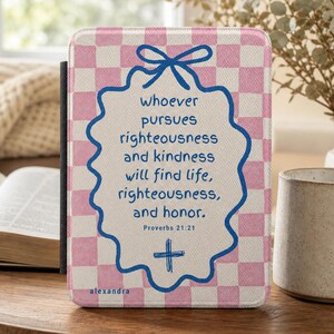 May include: A rectangular e-reader cover featuring a pink and white chequered pattern. The centre displays a blue scalloped-edge shape with a bow at the top, containing the text: whoever pursues righteousness and kindness will find life, righteousness, and honour. Proverbs 21:21, and a small cross symbol.