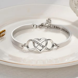 May include: Silver infinity heart bracelet with a row of clear crystals on the infinity symbol. The bracelet has an engraved message that reads "I love you mom".