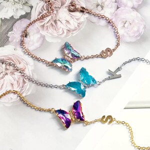 Könnte beinhalten: Drei zarte Armbänder mit Schmetterlingsanhängern und Initialanhängern. Die Armbänder sind aus goldenen, silbernen und roségoldenen Ketten gefertigt. Die Schmetterlinge sind aus schimmerndem Kristall und in Blau, Lila und Regenbogenfarben erhältlich.