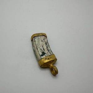 Puede incluir: Un pequeño colgante curvo hecho de hueso o marfil, con detalles dorados y un bucle para una cadena. El colgante tiene un aspecto natural y envejecido.
