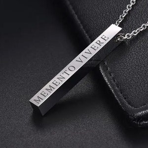 May include: A silver necklace with a rectangular pendant that reads "MEMENTO VIVERE".