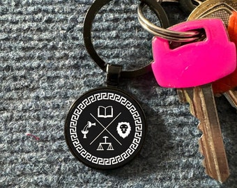 May include: Black metal keychain with a round, white design featuring a book, scales of justice, a chalice, and a lion's head. The design is surrounded by a white Greek key pattern.