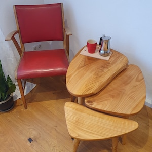 Könnte beinhalten: Drei verschachtelte Holztische mit einer einzigartigen, organischen Form. Der obere Tisch ist hellbraun mit einer roten Tasse und einer silbernen Kaffeekanne auf einem Holzbrett. Die Tische stehen auf einem hellen Holzboden.
