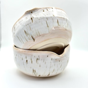 Könnte beinhalten: Ein Set aus drei Keramikbechern mit gesprenkelter, matter Oberfläche. Die Becher sind in Creme-, Hellgrau- und Dunkelgrautönen gehalten. Jeder Becher hat ein schlichtes, minimalistisches Design.