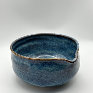 Könnte beinhalten: Eine handgefertigte Keramikschale mit tiefblauer Glasur und goldenem Rand. Die Schale hat eine einzigartige Form mit einem ausgießerartigen Merkmal auf einer Seite. Die Innen- und Außenflächen haben ein strukturiertes Aussehen.