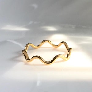 May include: A gold-colored wavy ring on a white surface.