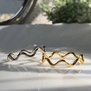 Może przedstawiać: Dwa faliste pierścienie, jeden srebrny, a drugi złoty, na białym tle.