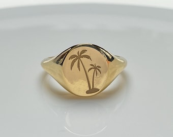 May include: A gold signet ring featuring an engraved palm tree design.