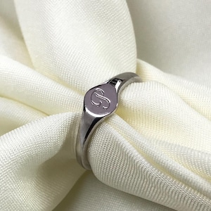 May include: A silver signet ring with a raised oval top featuring the letter "S" engraved on it.