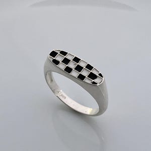May include: A silver ring with a black and white checkered oval design.