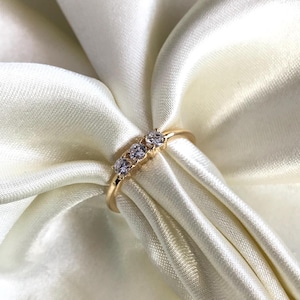 Op de afbeelding: Een gouden ring met drie kleine ronde, heldere stenen in een rij.