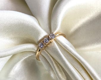 May include: A gold ring with three small round clear stones set in a row.