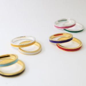 May include: A set of six gold rings with a thin band of enamel in different colors. The colors include red, blue, green, pink, yellow, and turquoise.
