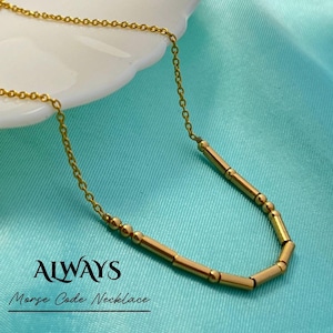Pode incluir: Um colar de código Morse dourado com a palavra "ALWAYS". O colar apresenta uma corrente delicada e contas cilíndricas e esféricas. O texto "Morse Code Necklace" está abaixo da palavra "ALWAYS".