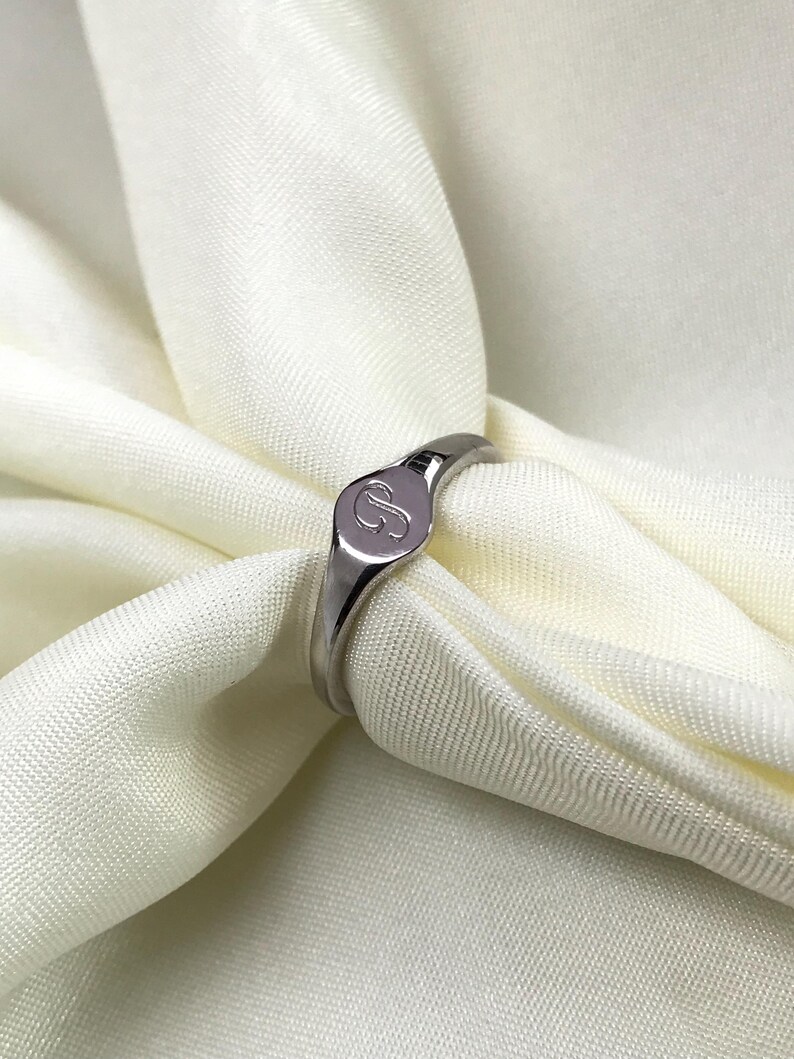 May include: A silver signet ring with a raised oval top featuring the letter "S" engraved on it.