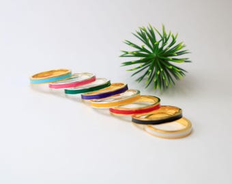 May include: A set of eight gold rings with a thin band of coloured enamel. The colours are turquoise, pink, green, purple, yellow, red, black, and white.