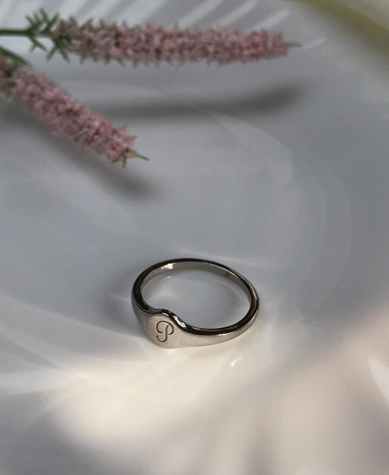 May include: A silver ring with a rounded oval top featuring the letter "S" engraved on the front.