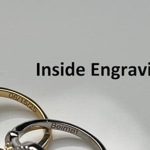 Pode incluir: Duas alian&ccedil;as de ouro com gravuras. A alian&ccedil;a de cima tem a data "06/15/25" gravada no interior. A alian&ccedil;a de baixo tem a palavra "Beimal" gravada no interior.