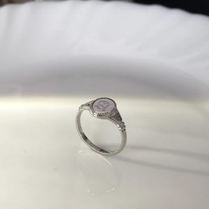 Pode incluir: Um anel de sinete de prata com uma parte superior ovalada em relevo que apresenta a letra "D".