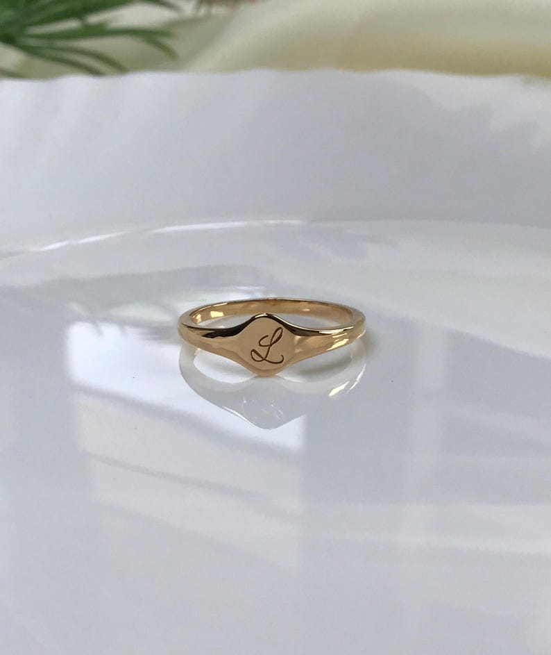 May include: A gold signet ring with a raised oval top featuring the letter "L" engraved on it.