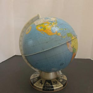 May include: A vintage tabletop globe featuring a blue ocean map with colorful continents and a meridian ring. The base is circular and decorated with black and white illustrations of the twelve zodiac signs, including Aries, Taurus, and Gemini.