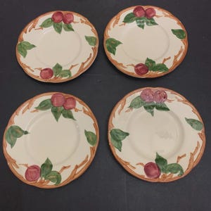 Op de afbeelding: Vier crèmekleurige keramische borden met een decoratieve rand van bruine takken, groene bladeren en rode vruchten. De borden zijn geplaatst op een donkere ondergrond, met een rustiek ontwerp.