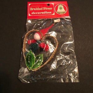May include: A braided straw heart-shaped Christmas ornament with a small elf doll inside. The ornament is packaged in a clear plastic bag with a red and white label that reads "Braided Straw decoration".