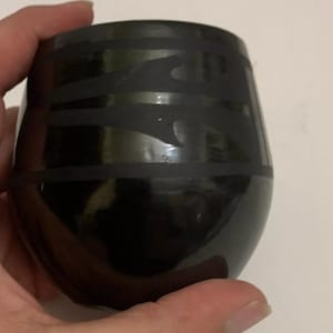 Puede incluir: Taza de cerámica negra con un diseño geométrico. La taza está pintada a mano con líneas y remolinos negros.