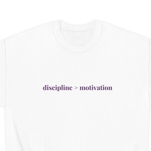 Op de afbeelding: Witte trui met de tekst "discipline > motivation" in paars op de voorkant.