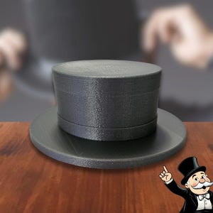 May include: A black top hat with a wide brim, made of a smooth, textured material. The hat is sitting on a wooden surface.