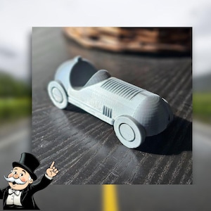 Può includere: Un'auto giocattolo grigia in stile vintage con un design dettagliato. L'auto ha una carrozzeria arrotondata e un solo sedile.