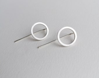 May include: A pair of silver earrings with a simple circle design. Each earring features a thin, straight post and a circular pendant with a hollow center.