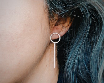 May include: Silver dangle earrings with a thin, vertical bar and a small circle at the top.