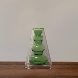 May include: A green glass vase with a bulbous shape and a clear glass base. The vase is sitting on a wooden surface.