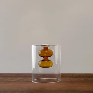 May include: A clear glass vase with a round, amber-colored glass orb inside. The orb is suspended in the center of the vase.
