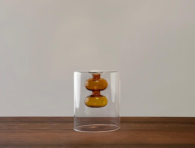 May include: A clear glass vase with a round, amber-colored glass orb inside. The orb is suspended in the center of the vase.