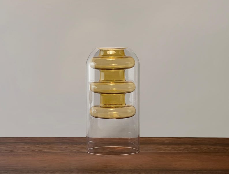 May include: A clear glass vase with three stacked, amber-colored glass rings. The vase is on a wooden surface.