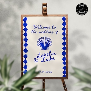Op de afbeelding: Een wit huwelijksbord met blauwe ruitpatronen aan de zijkanten. Het bord zegt "Welkom op de bruiloft van Lorelai & Luke" met een blauwe schelpgrafiek en de datum "20.09.2026".